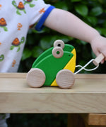 Child playing with the Bajo green double frogs pull along wooden toy, pulling it along the Miri slide.