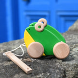 Bajo green double frogs pull along wooden toy placed on a stone wall. 