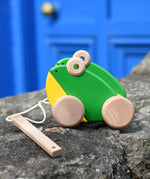 Bajo green double frogs pull along wooden toy placed on a stone wall. 