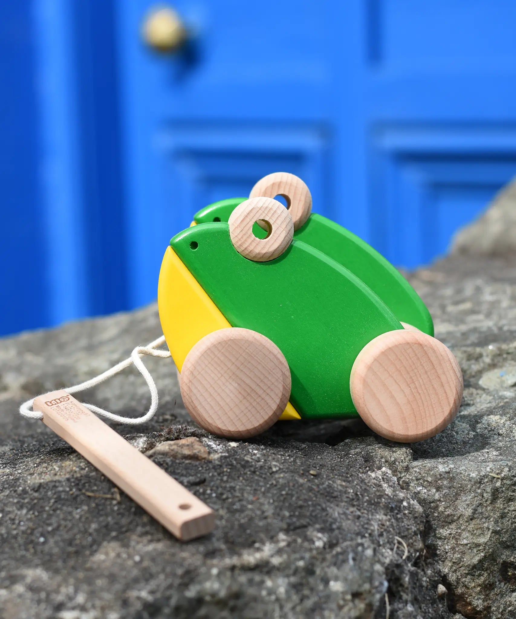 Bajo green double frogs pull along wooden toy placed on a stone wall. 