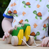 Child playing with Bajo green double frogs pull along toy, holding the wooden pull stick. 