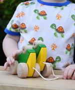 Child playing with Bajo green double frogs pull along toy, holding the wooden pull stick. 