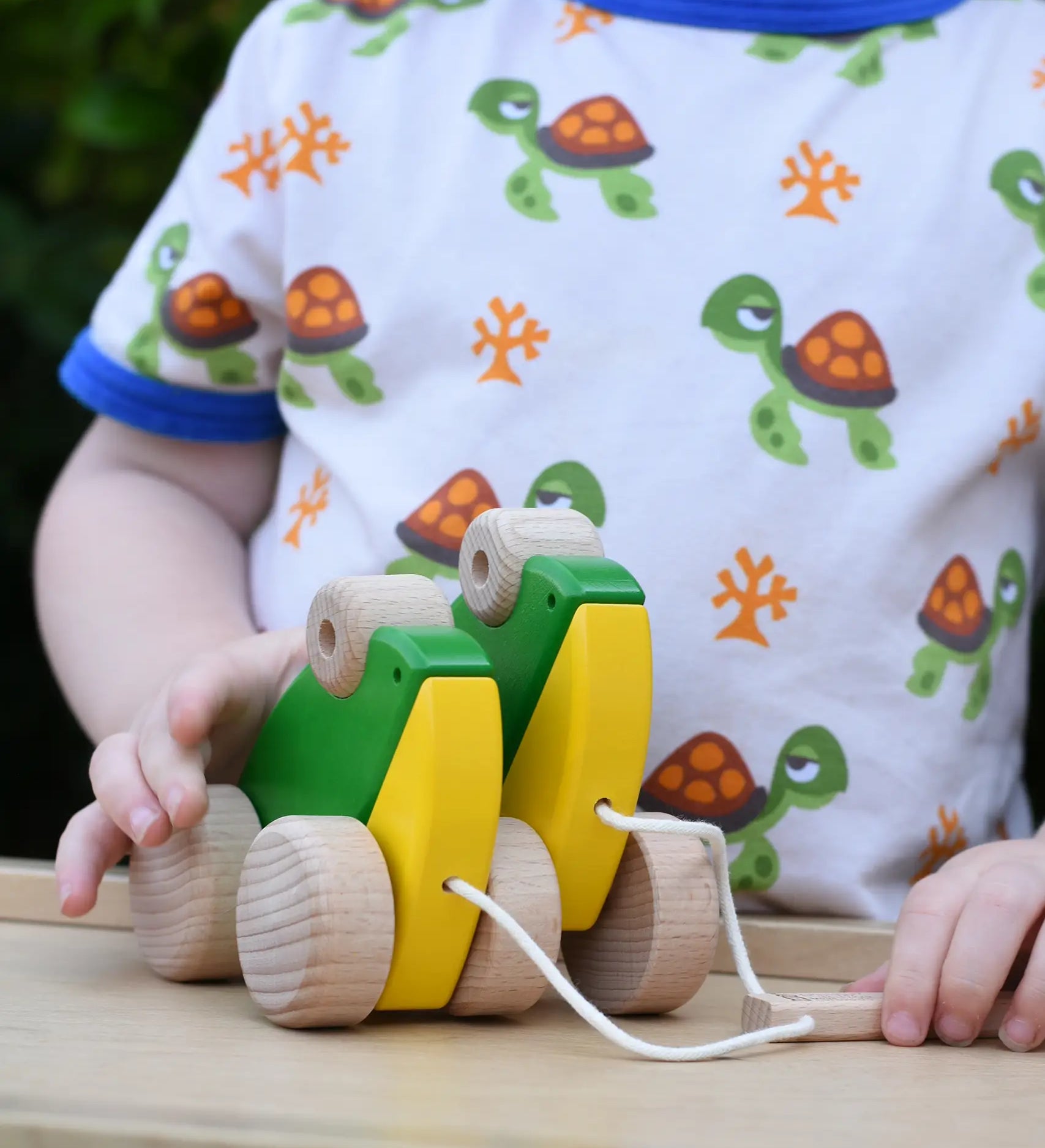 Child playing with Bajo green double frogs pull along toy, holding the wooden pull stick. 