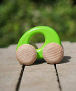Bajo handmade wooden ellipse toy car in green with unpainted wheels standing on a concrete surface
