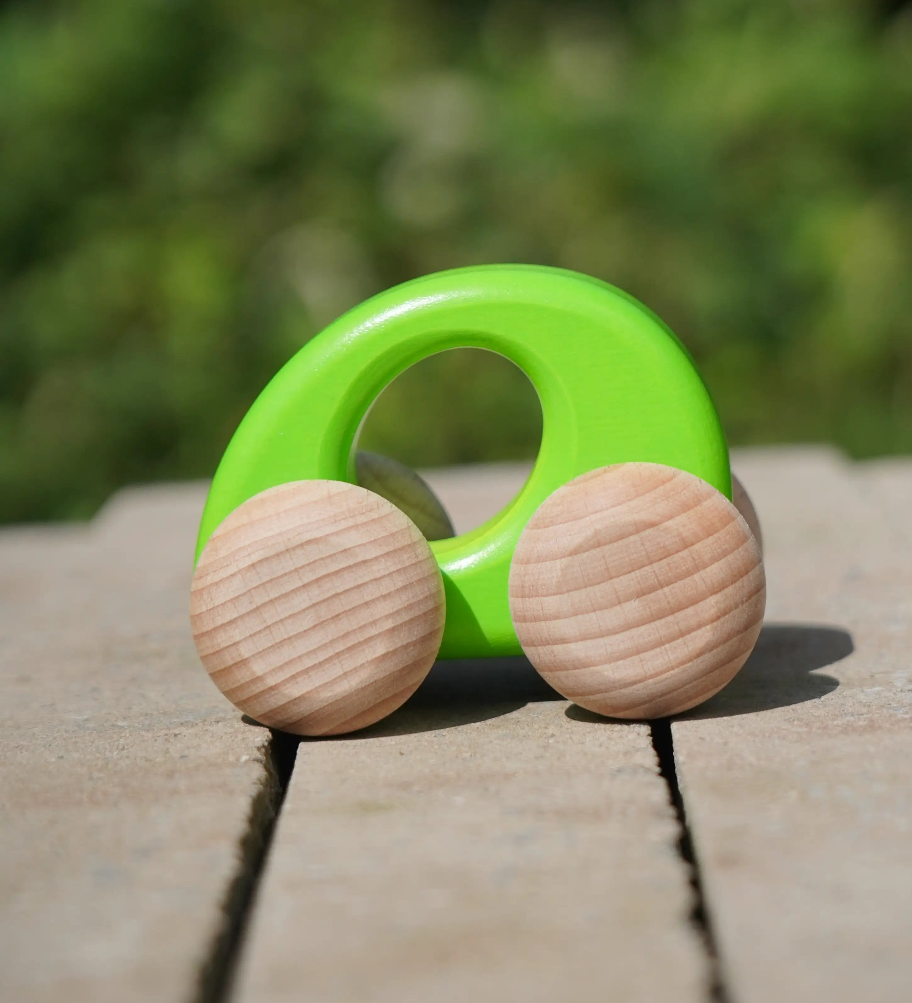 Bajo handmade wooden ellipse toy car in green with unpainted wheels standing on a concrete surface