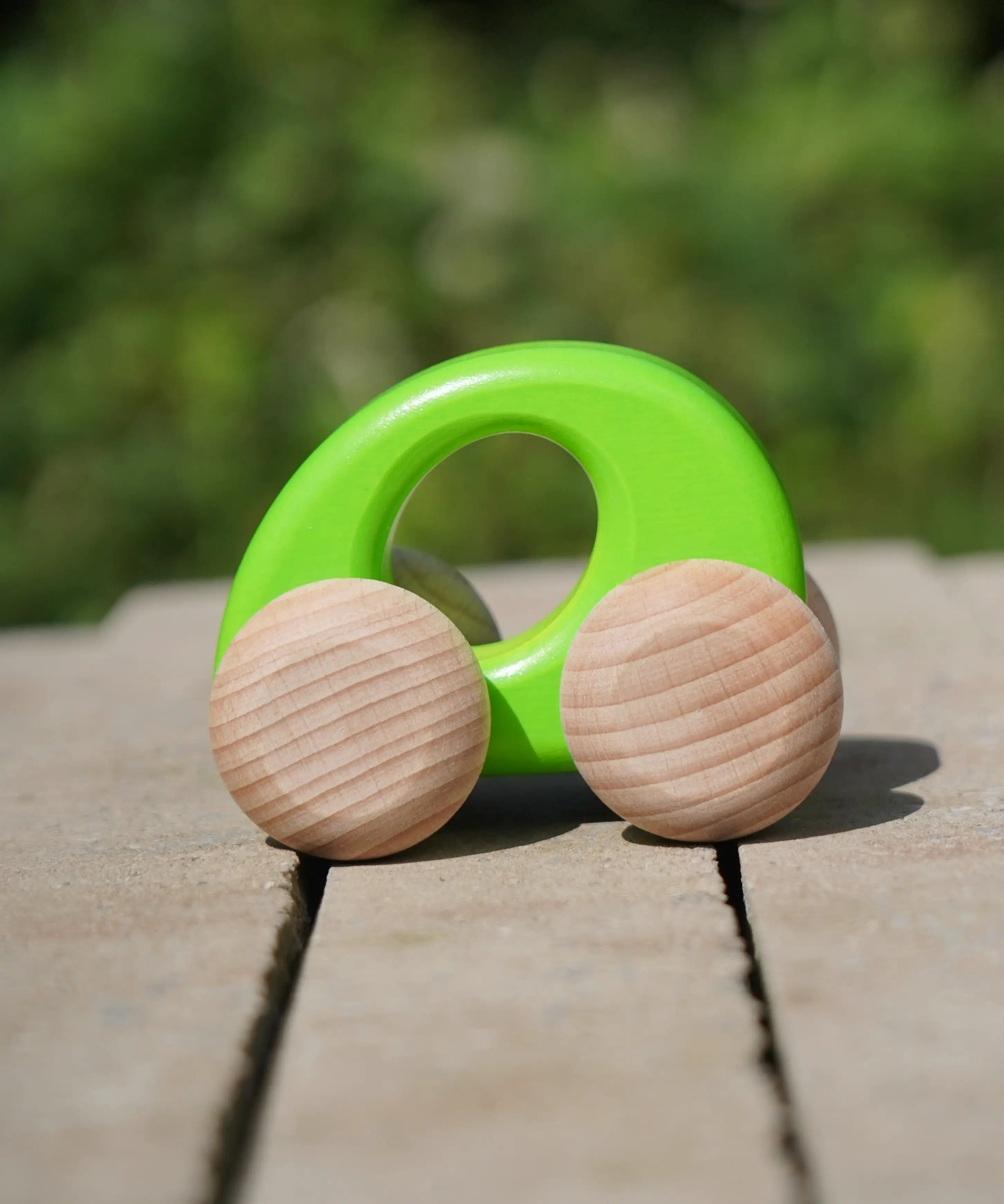 Bajo handmade wooden ellipse toy car in green with unpainted wheels standing on a concrete surface