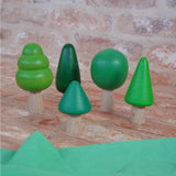 Bajo forest wooden toy tree figure set. Five green trees in different heights and shapes. Green laura's play cloth can be seen in the foreground.