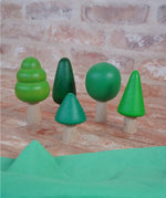 Bajo forest wooden toy tree figure set. Five green trees in different heights and shapes. Green laura's play cloth can be seen in the foreground.