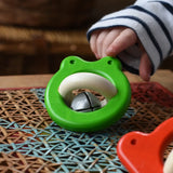 Bajo green Frog Rattle wooden baby toy placed on a rattan stool in the Babipur playroom, a child is pointing at it in the background..