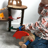 A child holding the Bajo blue pull along dragon wooden toy.  The dragon toy features two wheels at the front and back and red wing that move along with the front wheels. These heirloom quality toys by Bajo are part of a wide range of wooden toys available here at Babipur.