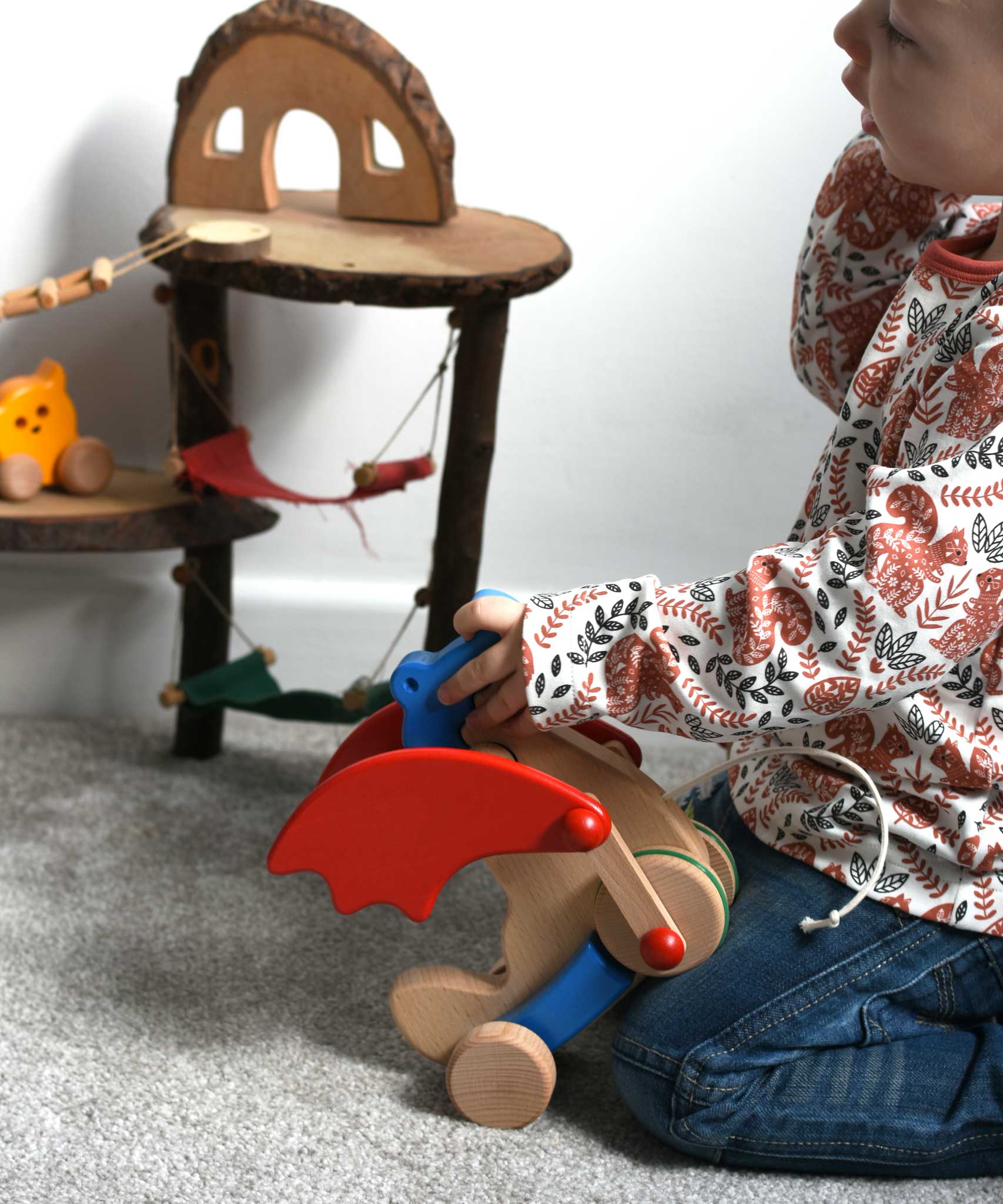 A child holding the Bajo blue pull along dragon wooden toy.  The dragon toy features two wheels at the front and back and red wing that move along with the front wheels. These heirloom quality toys by Bajo are part of a wide range of wooden toys available here at Babipur.