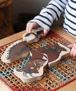 Child playing with Bajo Gruffalo character puzzle on a rattan stool in the Babipur playroom.