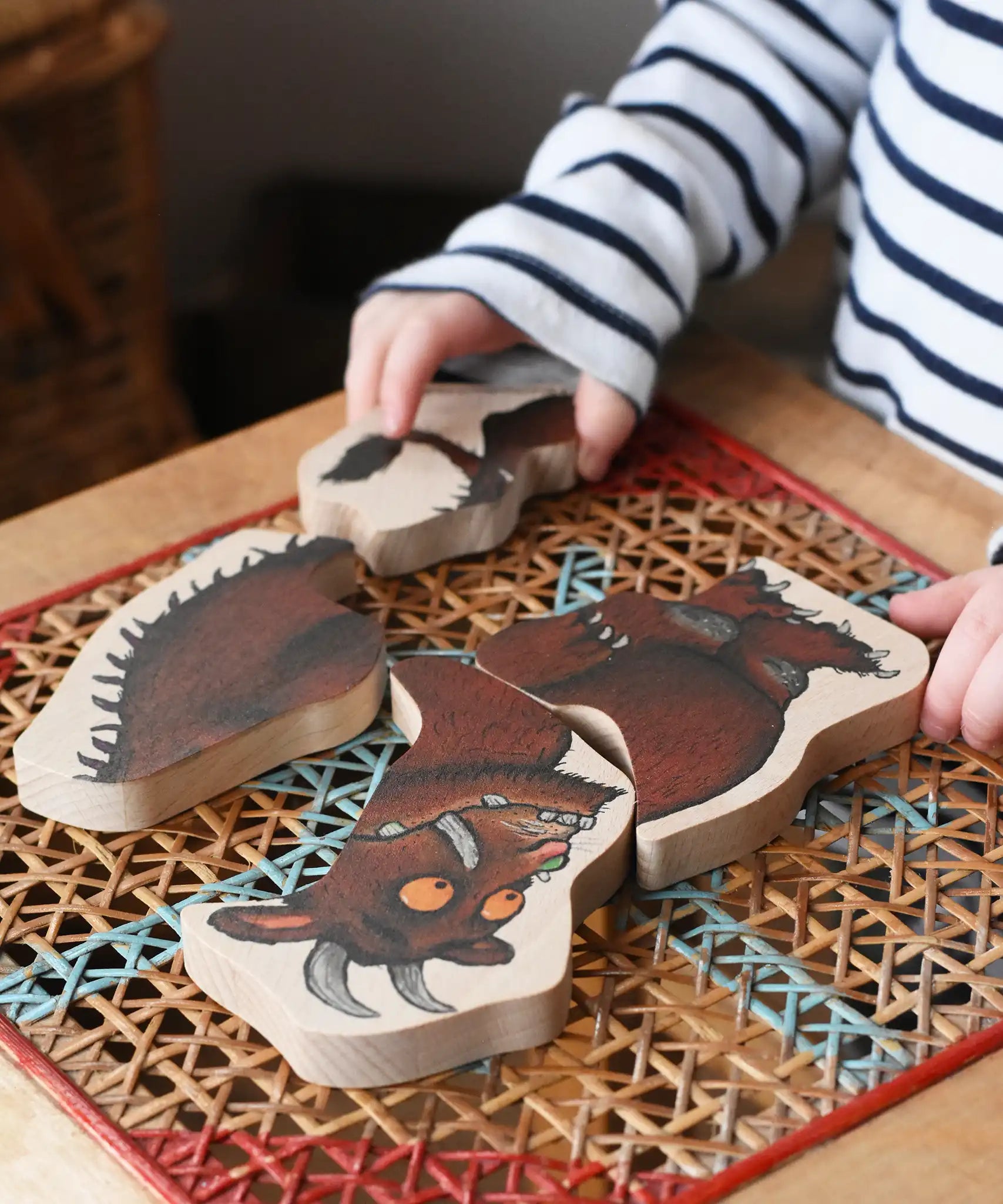 Child playing with Bajo Gruffalo character puzzle on a rattan stool in the Babipur playroom.