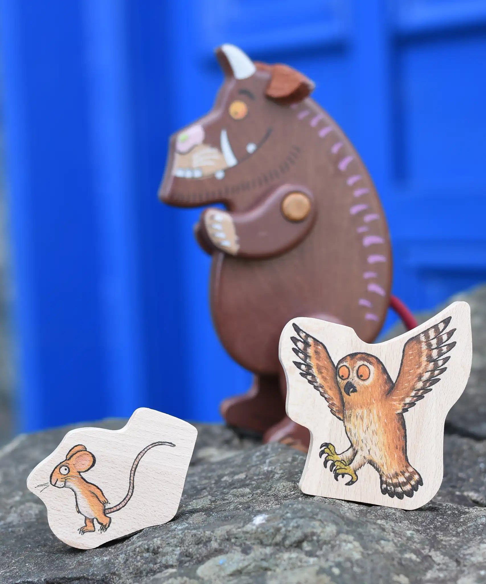 Mouse and owl pieces from the Bajo Gruffalo Character Puzzle placed on a stone wall in front of the Gruffalo figure.