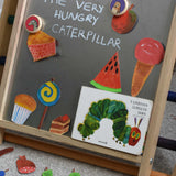A snake and owl Bajo magnet placed on the Triclimb biri board with hand drawn food featured in the very hungry caterpillar book. These magnets are part of a range of Bajo wooden toys available at Babipur. 