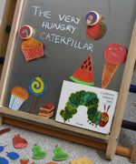 A snake and owl Bajo magnet placed on the Triclimb biri board with hand drawn food featured in the very hungry caterpillar book. These magnets are part of a range of Bajo wooden toys available at Babipur. 