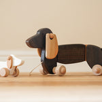 Bajo wooden dachshund puppy next to a pull along dachshund toy figure on a wooden floor