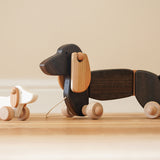 Bajo wooden dachshund puppy next to a pull along dachshund toy figure on a wooden floor