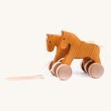 Bajo hand made wooden jumping horse in natural and available at Babipur. Features unpainted wheels  and a toggle to pull along the horses