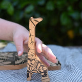 Child's hand reaching for the giraffe shaped piece from the Bajo jungle puzzle.