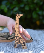 Child's hand reaching for the giraffe shaped piece from the Bajo jungle puzzle.