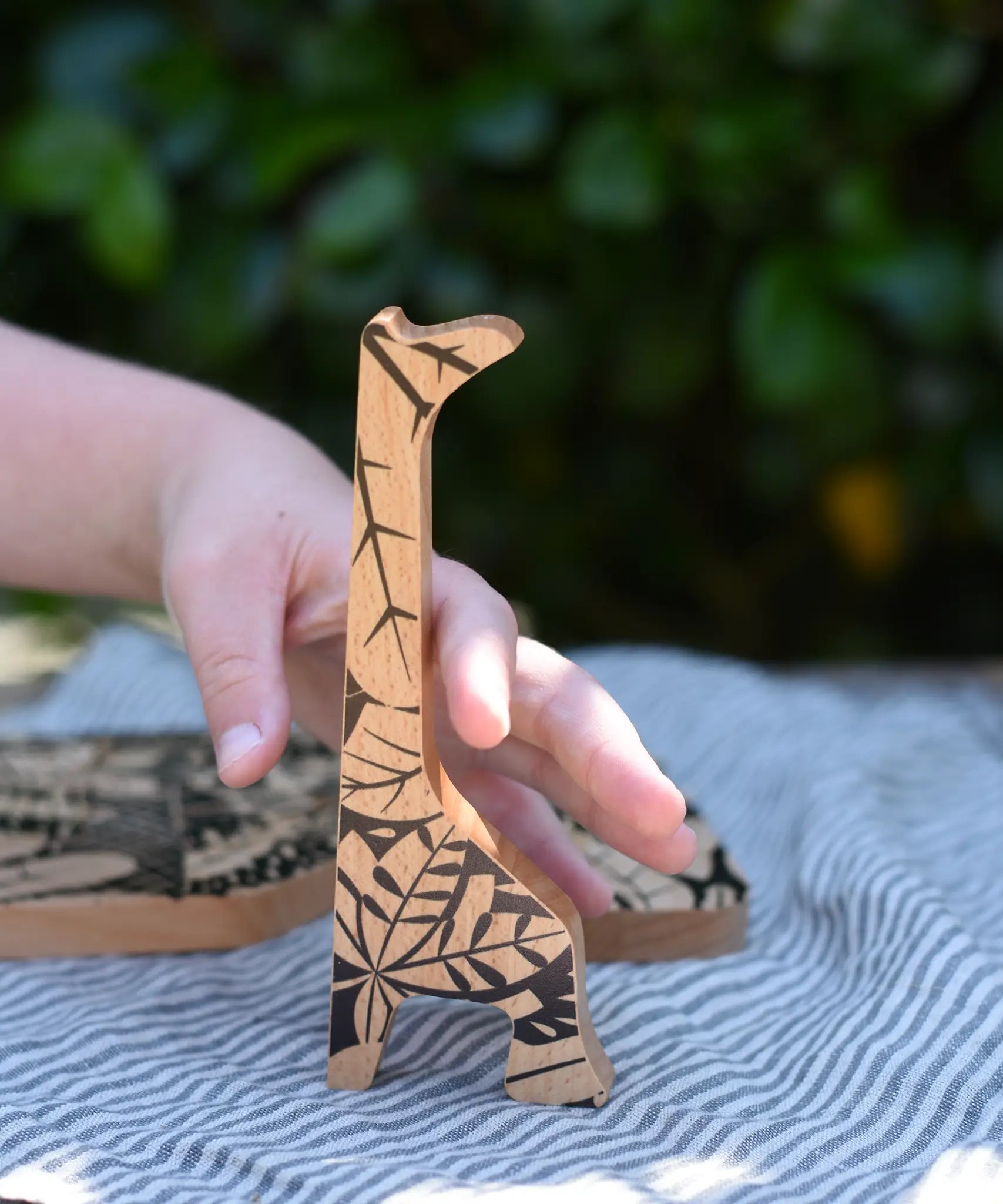 Child's hand reaching for the giraffe shaped piece from the Bajo jungle puzzle.