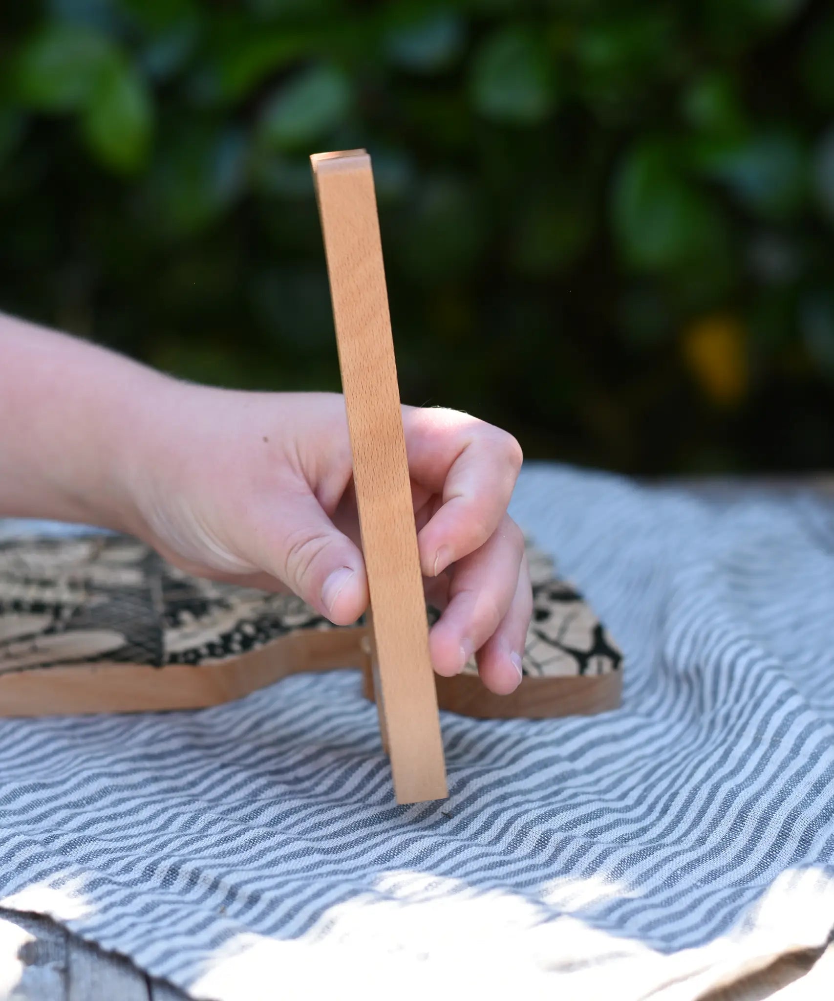 Child's hand holding for the giraffe shaped piece from the Bajo jungle puzzle showing the side.