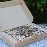 Bajo jungle puzzle with black pattern on natural wood shown in it's cardboard packaging box.