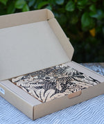 Bajo jungle puzzle with black pattern on natural wood shown in it's cardboard packaging box.