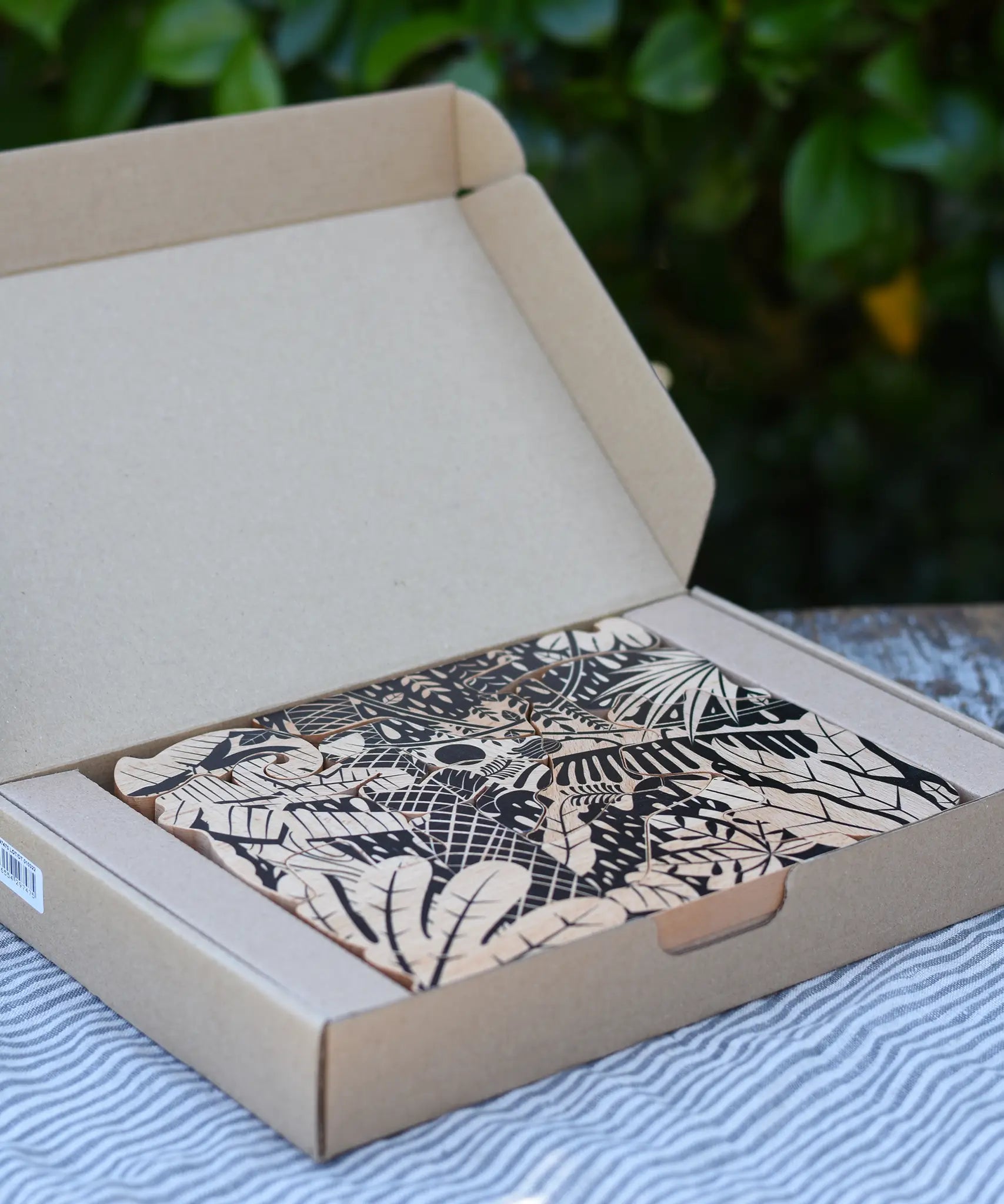 Bajo jungle puzzle with black pattern on natural wood shown in it's cardboard packaging box.