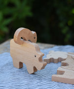 Bajo jungle puzzle , wooden animal shaped pieces one side plain natural wood, one side with a black pattern. Chameleon shaped pieced placed balancing on top of the rhino piece.