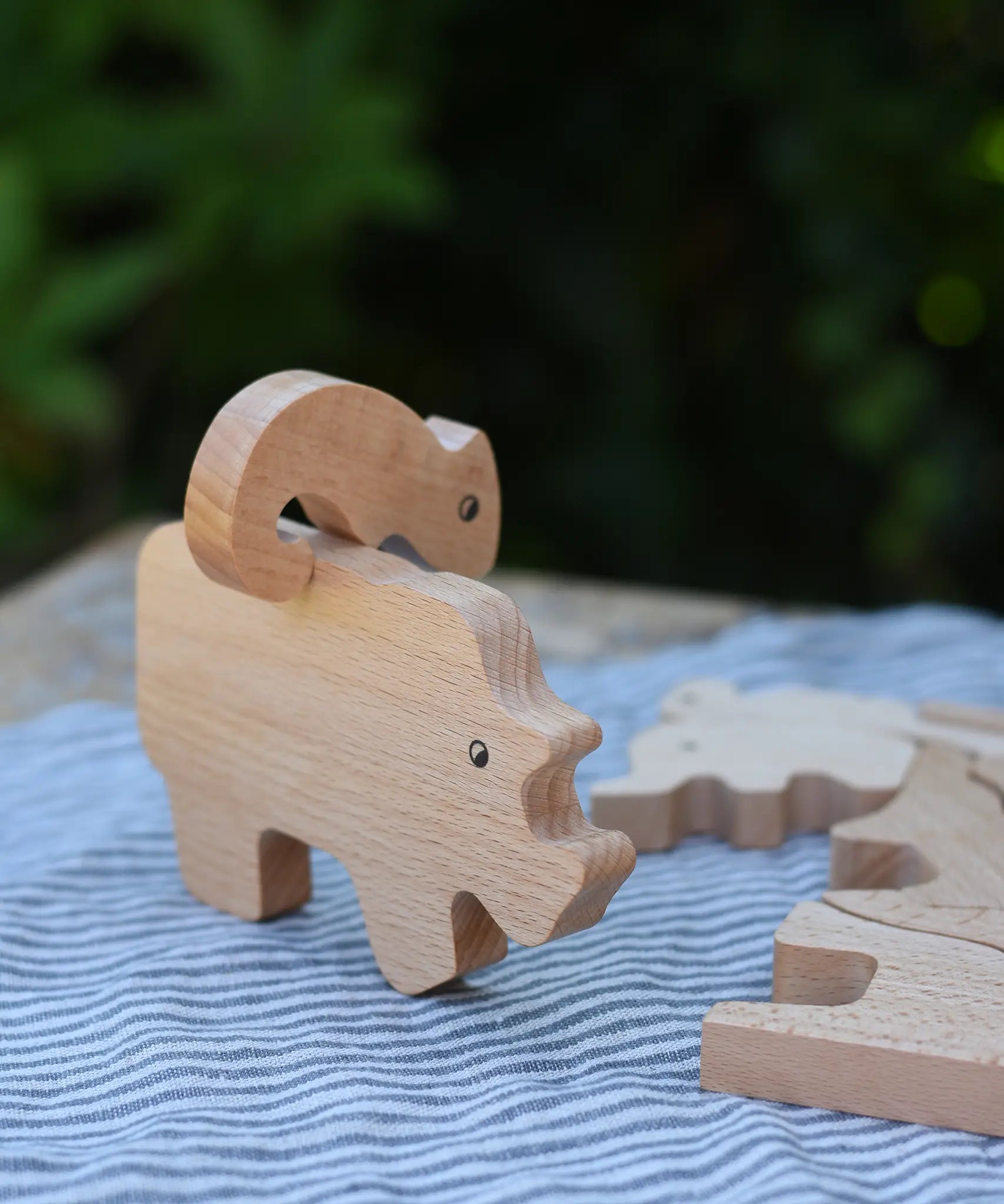Bajo jungle puzzle , wooden animal shaped pieces one side plain natural wood, one side with a black pattern. Chameleon shaped pieced placed balancing on top of the rhino piece.