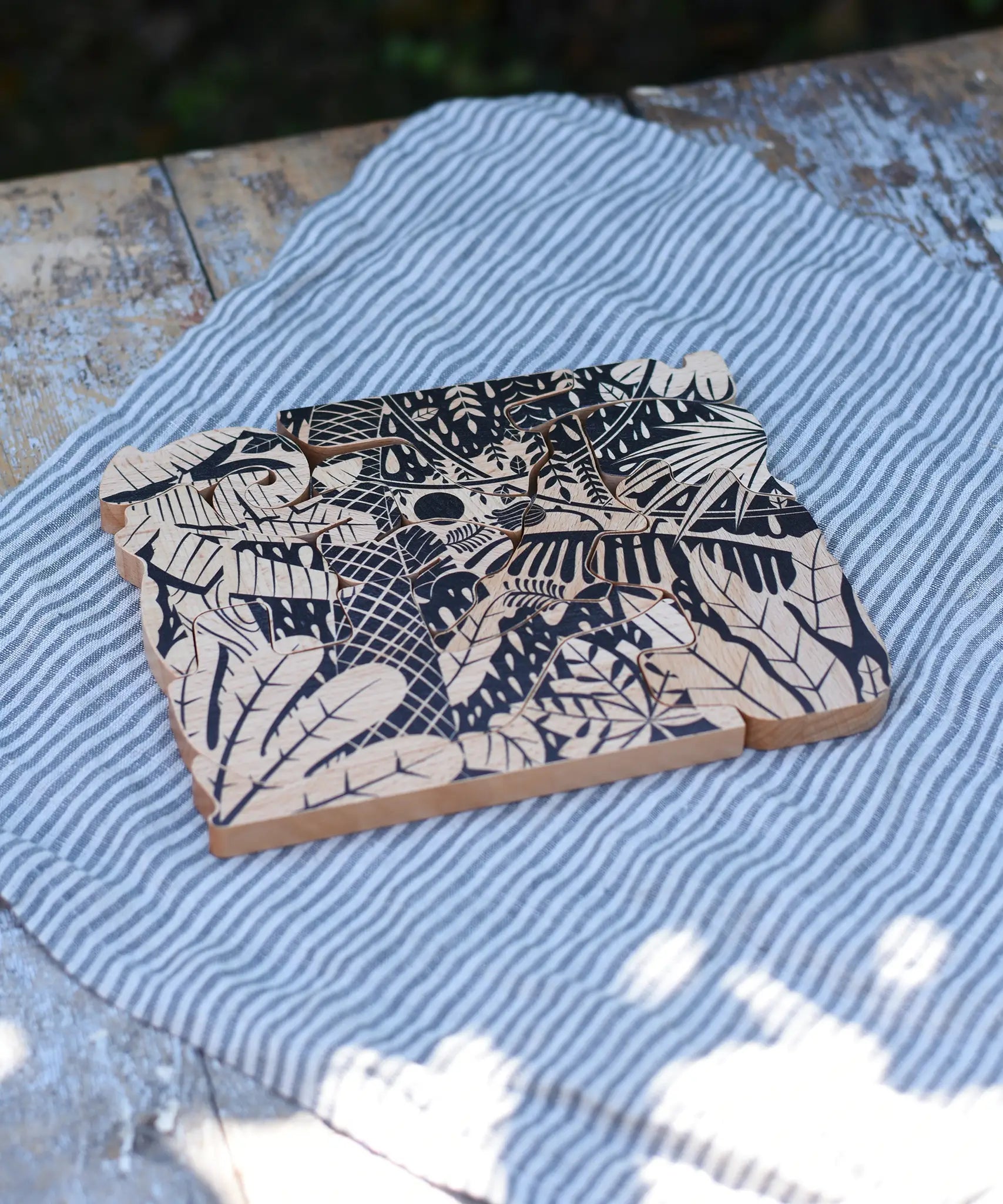 Bajo jungle puzzle shown on the black patterned side. Puzzle is made up of different animal shaped pieces.
