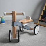 A Bajo Toys wooden Cycle toddler Ride-On in the monochrome, white and grey colourway placed on a carpeted surface. The wooden ride on cycle is part of a wode range of wooden toys available here at Babipur. 