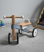 A Bajo Toys wooden Cycle toddler Ride-On in the monochrome, white and grey colourway placed on a carpeted surface. The wooden ride on cycle is part of a wode range of wooden toys available here at Babipur. 