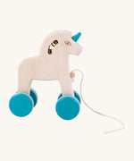 The Tobe Pull Along Unicorn, with almost white coloured wood showing off the rich grain of real wood, and turquoise blue painted wheels and turquoise horn. The image also shows the bells inside the unicorn head, and the pull cord to pull along the unicorn. The image is on a cream background
