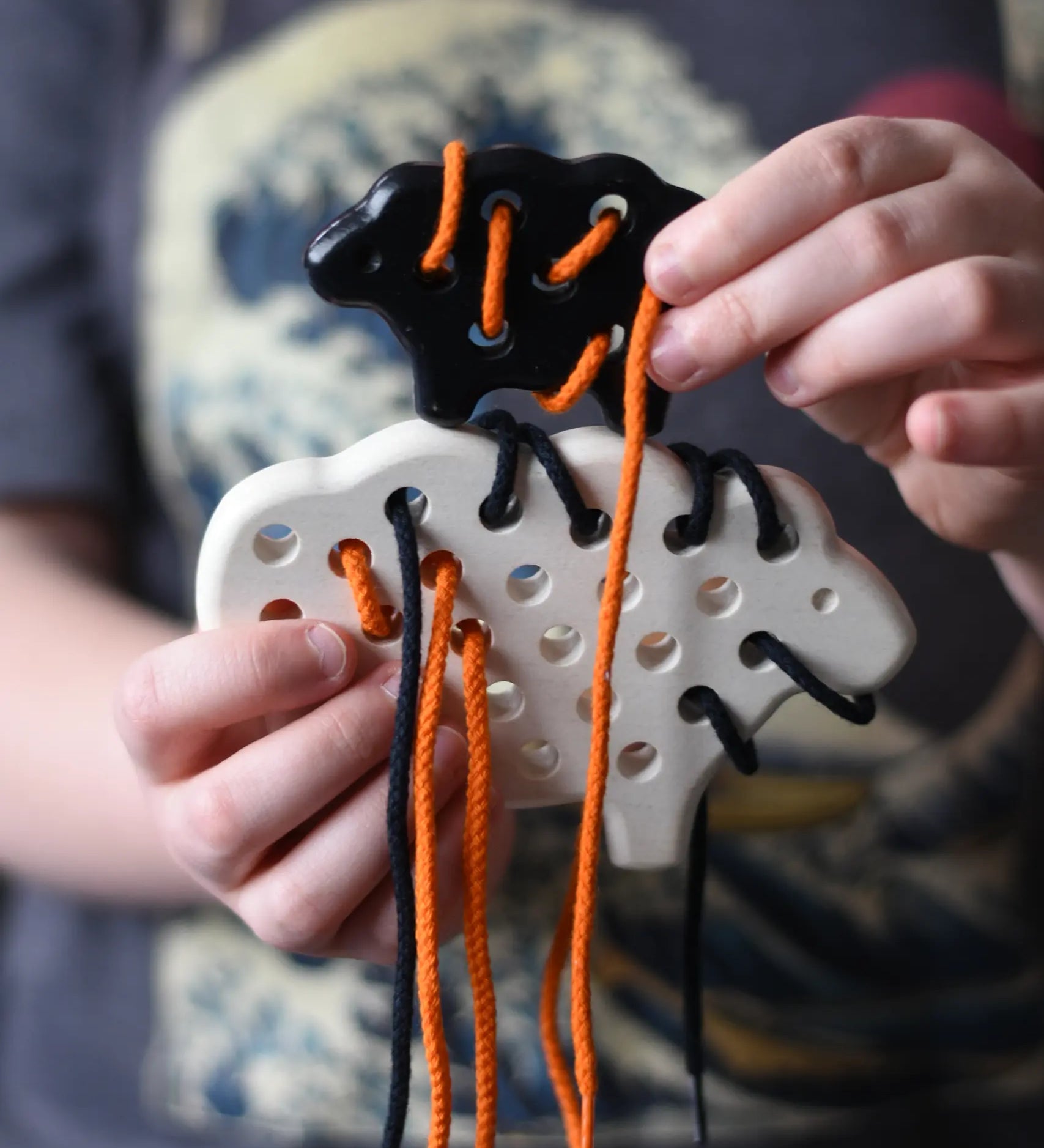 Bajo wooden lacing sheep and lamb toy with orange and black laces in a child'd hands.