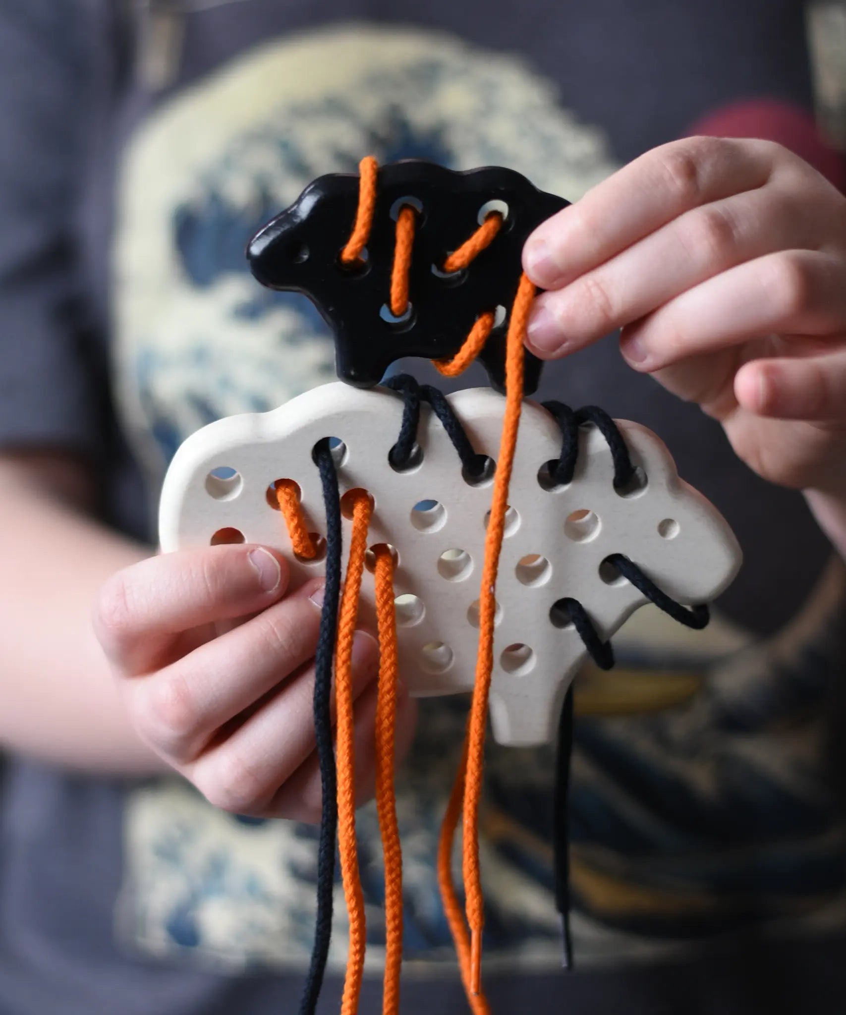 Bajo wooden lacing sheep and lamb toy with orange and black laces in a child'd hands.