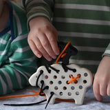 Bajo wooden lacing sheep and lamb toy with orange and black laces. Child placing the black lamb on the white sheep.