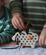 Bajo wooden lacing sheep and lamb toy with orange and black laces. Child placing the black lamb on the white sheep.