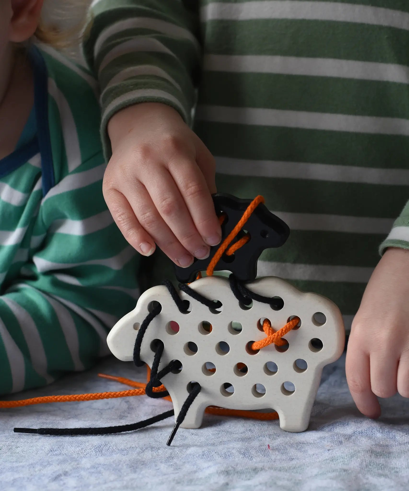 Bajo wooden lacing sheep and lamb toy with orange and black laces. Child placing the black lamb on the white sheep.