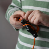 Bajo wooden lacing black lamb toy with orange lace, child's hand threading the lace through the holes.