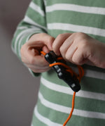 Bajo wooden lacing black lamb toy with orange lace, child's hand threading the lace through the holes.