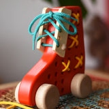 Front of the Bajo red lacing shoe wooden push along toy placed on a rattan stool in the Babipur playroom.
