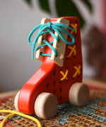 Front of the Bajo red lacing shoe wooden push along toy placed on a rattan stool in the Babipur playroom.