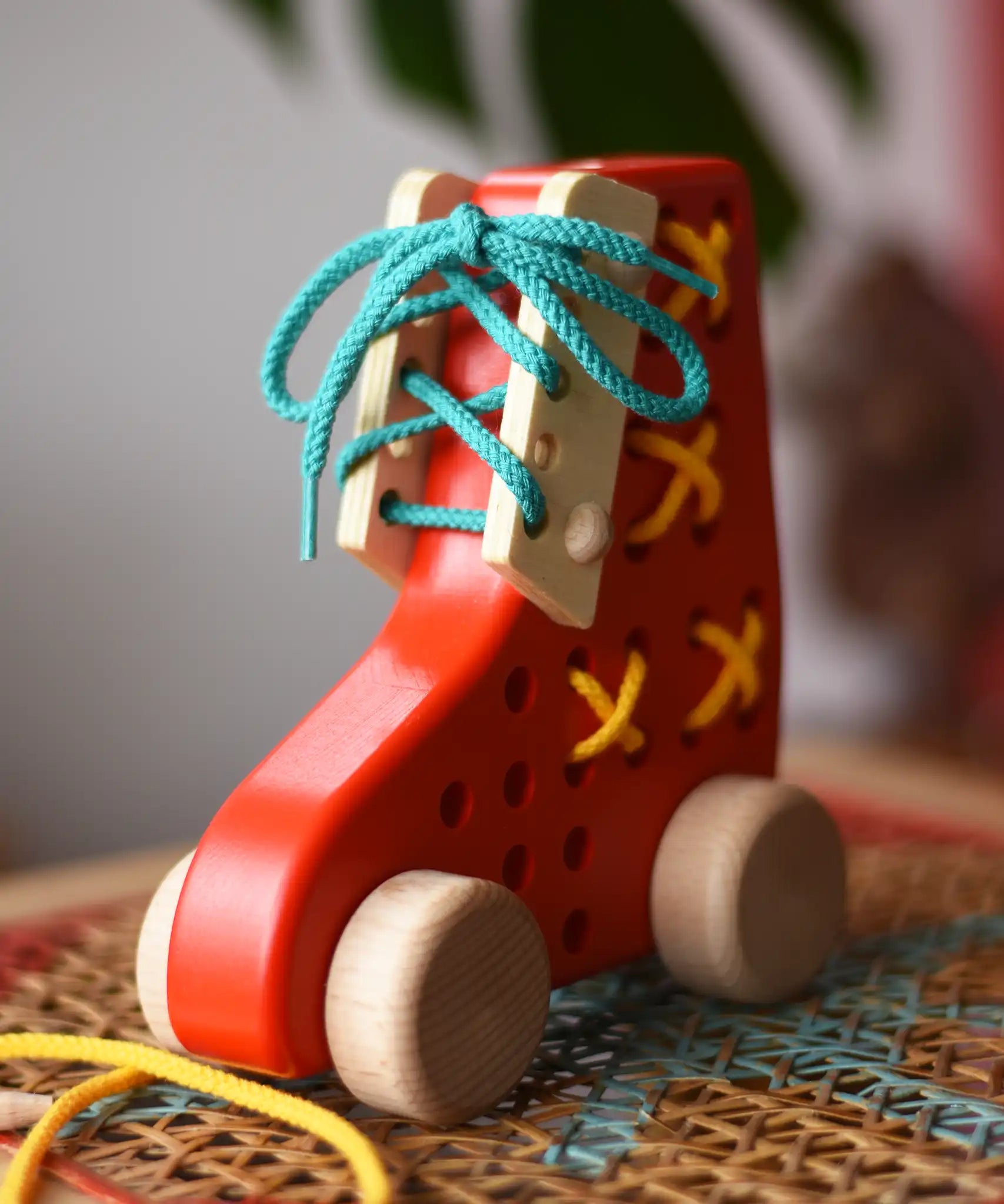 Front of the Bajo red lacing shoe wooden push along toy placed on a rattan stool in the Babipur playroom.