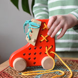 Child playing with the Bajo red lacing shoe wooden push along toy placed on a rattan stool in the Babipur playroom.