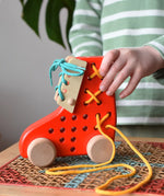 Child playing with the Bajo red lacing shoe wooden push along toy placed on a rattan stool in the Babipur playroom.