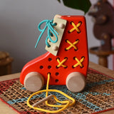 Side of the Bajo red lacing shoe wooden push along toy placed on a rattan stool in the Babipur playroom.