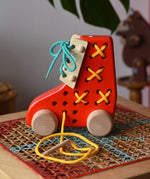 Side of the Bajo red lacing shoe wooden push along toy placed on a rattan stool in the Babipur playroom.